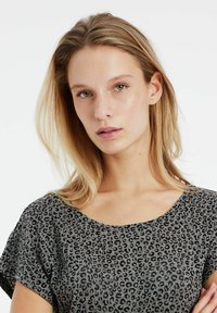 Top gris de manga corta con un estampado de leopardo negro, que presenta un escote ancho y un tejido suave y texturizado.