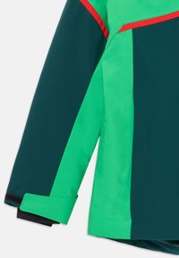 Grønn og mørk teal jakkearm med en rød aksentlinje, spesielt med en Borrelås-lukking i mansjetten og glatt, strukturert stoff.