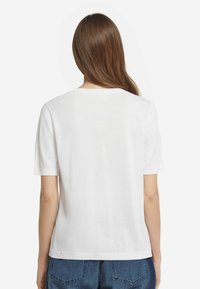 Hvid kortærmet t-shirt med rund hals. Fremstillet af glat stof med en afslappet pasform og enkel kant. Ingen synlige mønstre eller detaljer.