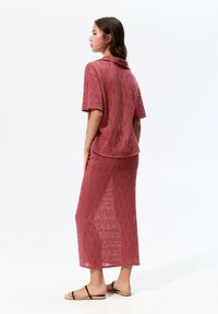 Twee-delig outfit in een textuurstof van lichtgewicht, met een kort mouw colbert en een lange rok, beide in een gedempte rozenkleur.