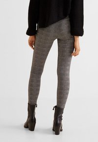 Legginsy w szaro-czarną kratkę wykonane z elastycznego materiału, z wysokim stanem i dopasowanym krojem, zestawione z czarnymi botkami za kostkę.