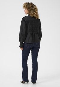 Maglietta nera a maniche lunghe con schiena arricciata, caratterizzata da maniche a sbuffo. Abbinata a jeans flare blu scuro e scarpe con tacco.