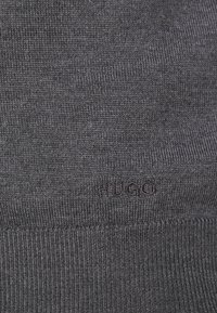 Donkergrijze gebreide stof met een gladde textuur, voorzien van een subtiele "HUGO" logo gestikt in een donkerdere draad nabij de onderrand.