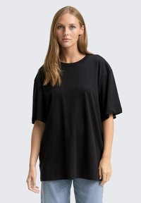 Zwarte oversized t-shirt van katoen. Heeft korte mouwen en een ronde halslijn. Subtiele versieringen creëren een gestructureerd patroon.