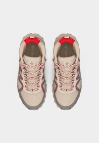 Ζευγάρι μπεζ και κόκκινων παπουτσιών ορειβασίας Columbia με κορδόνια με μοτίβο, ύφασμα από δίχτυ και παχιά, ανθεκτική σόλα, φαίνονται από πάνω.