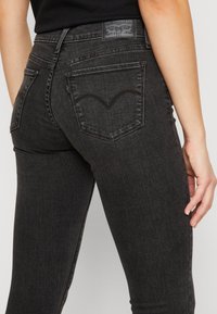 Jeans de mezclilla negra con un diseño ajustado, que cuentan con una distintiva costura curvada en el bolsillo trasero y una etiqueta de cuero con marca en la cinturilla.