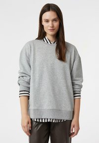 Szara bluza o luźnym kroju, z żebrowanym kołnierzem i długimi rękawami, noszona na czarno-białej koszuli w paski. Gładka tekstura materiału.