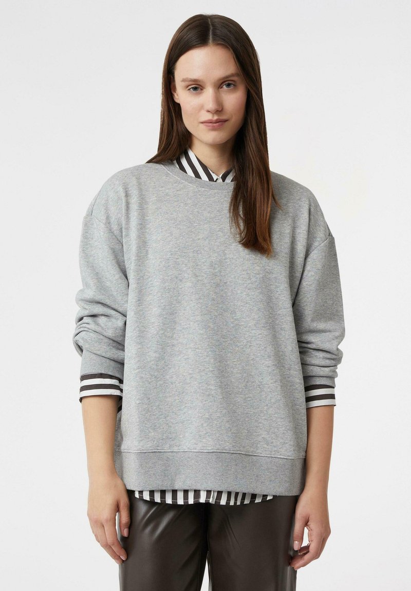 Szara bluza o luźnym kroju, z żebrowanym kołnierzem i długimi rękawami, noszona na czarno-białej koszuli w paski. Gładka tekstura materiału.