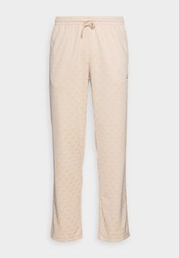 Beige tepláky vyrobené z měkkého materiálu, s celoplošným vzorem listů, elastickým pasem se šňůrkou a bočními kapsami.