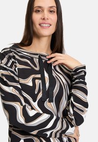 Black sweatshirt with abstract wave patterns in beige, cream, and gray. Features a hood with elasticated black drawstrings and ribbed cuffs.