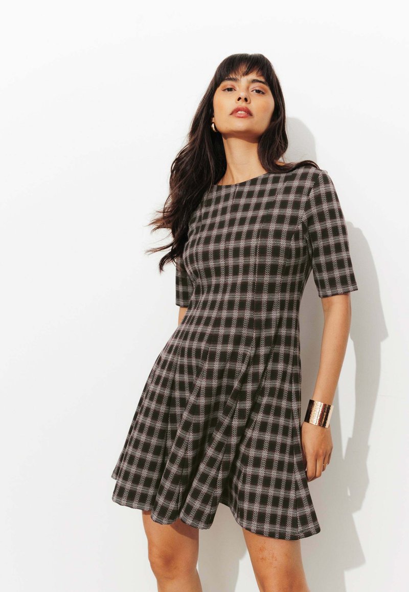 Robe à carreaux noir et blanc avec des manches courtes et une jupe évasée. Présente un col rond et une texture lisse.