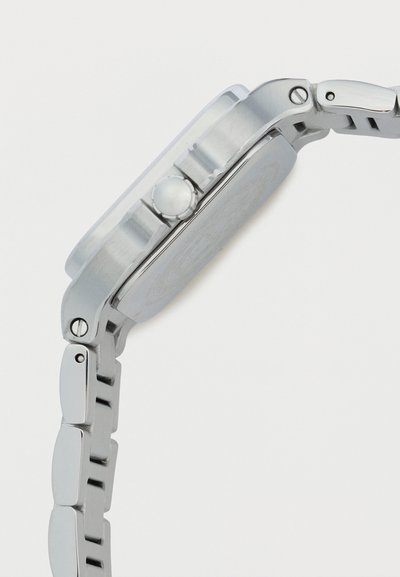 Πλευρική όψη ασημένιου μεταλλικού ρολογιού που δείχνει στρογγυλεμένο κορόνα και συνδεδεμένο μπρασελέ σε λευκό φόντο.