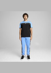 Tenue de sport noire et bleu clair avec un t-shirt à manches courtes et un pantalon de survêtement. Le t-shirt porte le logo PUMA ; le pantalon a des bandes latérales noires.