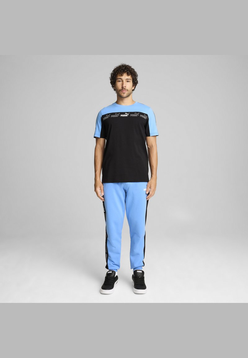 Tenue de sport noire et bleu clair avec un t-shirt à manches courtes et un pantalon de survêtement. Le t-shirt porte le logo PUMA ; le pantalon a des bandes latérales noires.