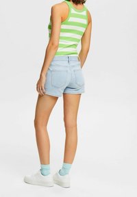 Shorts de mezclilla azul claro con cintura alta y diseño de cuatro bolsillos, combinados con una camiseta sin mangas de rayas verdes y blancas. Zapatillas blancas y calcetines azul claro.