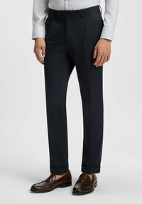 Marina byxor med skräddarsydd passform, försedda med dubbla veck, sidofickor och en slät yta. Bärs med bruna läderloafers.