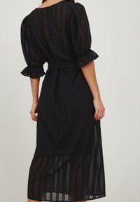 Černé midi šaty z průsvitné texturované látky; nabírané rukávy; pas s páskem; vrstvený design. Vertikální pruhy vytvářejí jemný vzor.