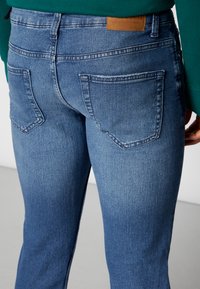 Ferdige blå denimjeans med middels vask, med en klassisk fem-lomme design og et brunt lærmerke på livet.