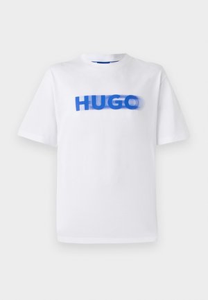 Balts kokvilnas T-kreklus ar apaļu kaklu, kura priekšpusē ir liels zils grafikas attēls ar vārdu "HUGO", nedaudz izplūdis efekts.