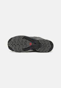 Suola di scarpa outdoor nera con un profilo di battistrada profondo e accento rosso. Il materiale in gomma garantisce trazione, caratterizzato da un design robusto e multidirezionale.