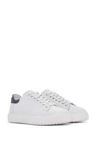 Un par de zapatillas blancas de caña baja con cordones blancos y acentos negros en el talón, mostradas una al lado de la otra sobre un fondo blanco.