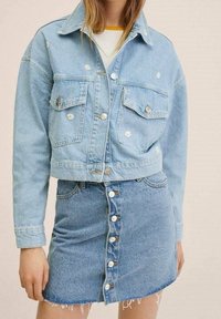 Ljusblå denimjacka med broderade blommor, i kombination med en matchande denimkjol med knappar och fransad fåll.