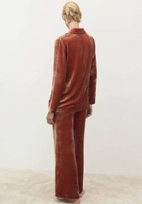 Set di pigiama in velluto color ruggine; presenta una camicia a maniche lunghe con colletto e pantaloni a gamba larga abbinati, con una finitura morbida e testurizzata.