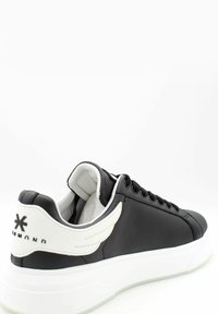 Zapatilla deportiva negra de perfil bajo con suela blanca, detalle blanco en forma de ala y logo de la marca "Diamond" en el talón, vista angulada hacia la izquierda, sobre fondo blanco.