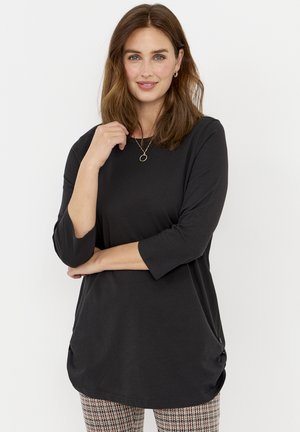 Zwarte top met lange mouwen en een ronde halslijn, zachte textuur en ruching aan de zijkanten. Gemaakt in combinatie met een broek met een patroon en een ruitmotief.
