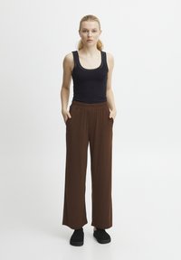 Brown wide-leg pants with an elastic waistband and side pockets, paired with a black tank top. The material appears soft and comfortable.