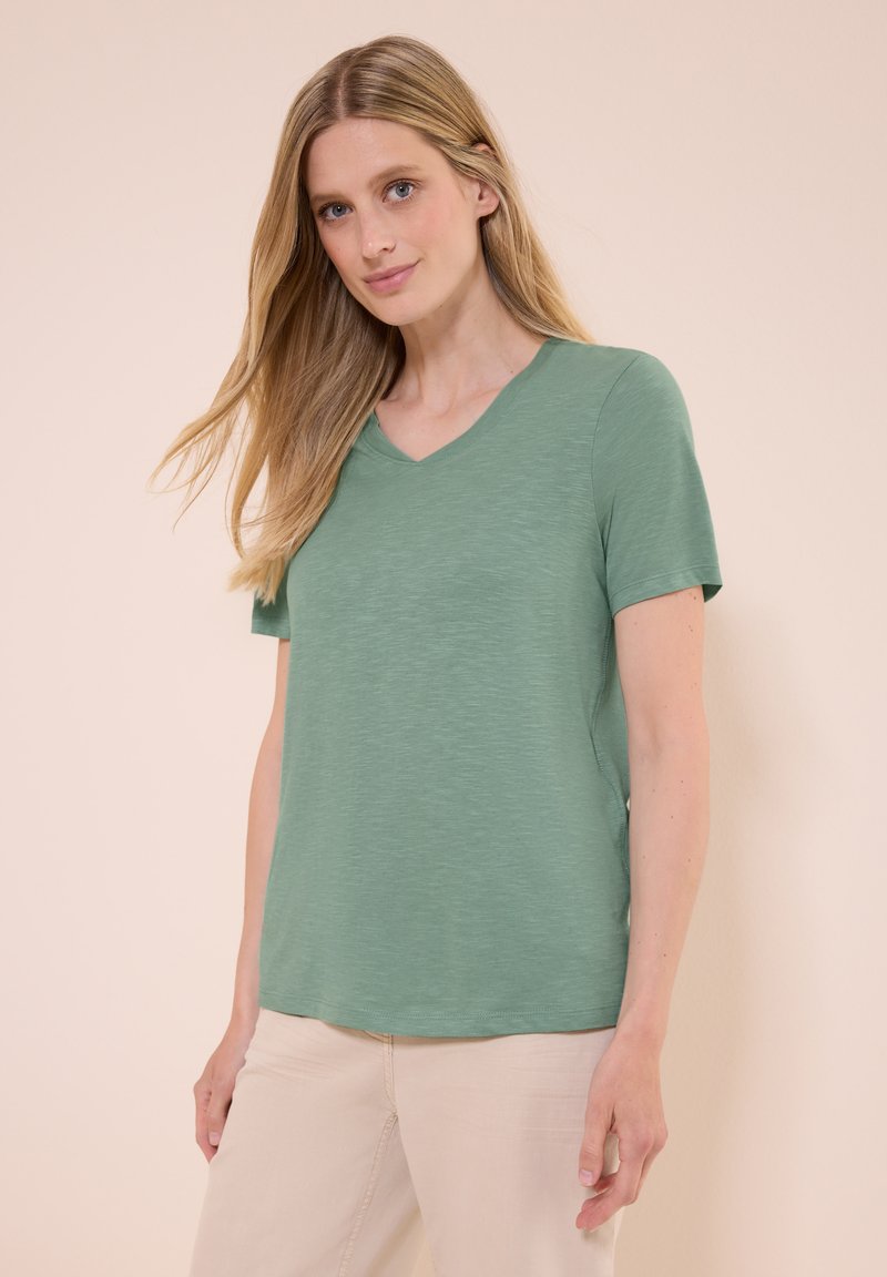 T-shirt a maniche corte, con scollo a V in verde tenue, realizzato in tessuto morbido e leggero con una leggera finitura testurizzata. Taglio semplice e comodo.
