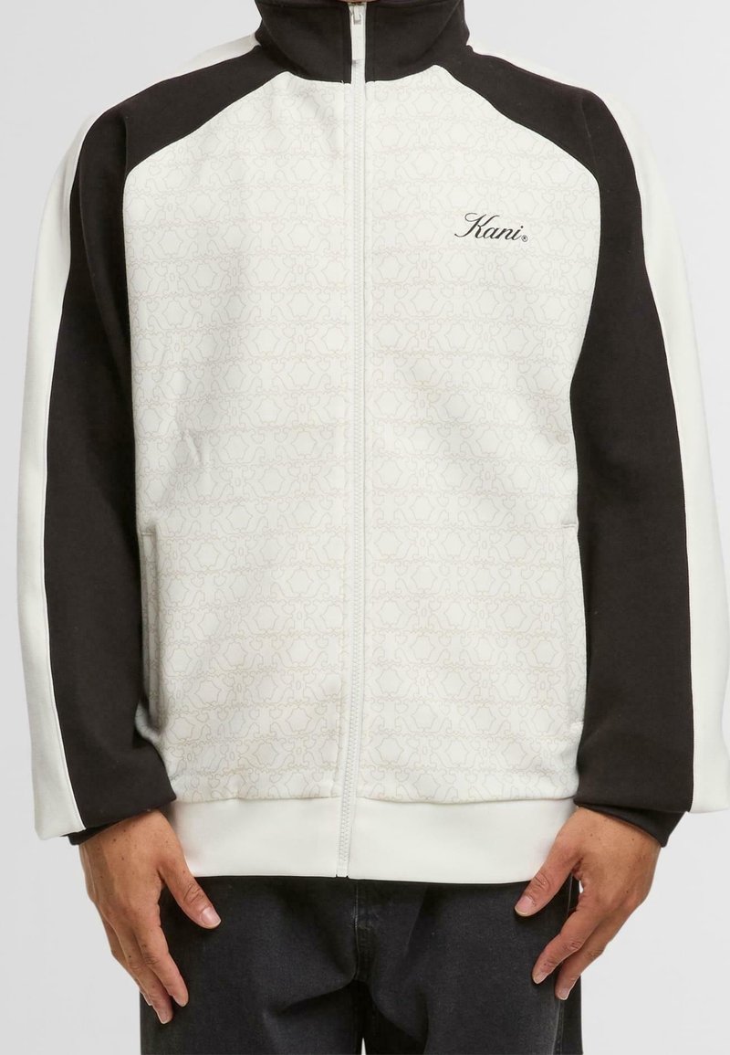 Zip-up jacket with a white body featuring a textured pattern, black sleeves, and white accents. "Kani" logo on the chest. Soft material.