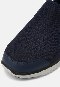 Sötétkék hálós slip-on cipő, amely texturált felülettel, tartós szintetikus díszítésekkel és fehér gumitalppal rendelkezik, szürke díszítéssel.