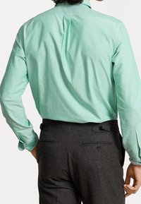 Mintgrön långärmad skjorta med slät textur och spetsig krage, kombinerad med mörkgrå byxor med sidjusterare och fickor.