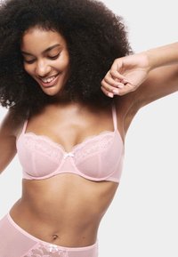 Lichtroze beha met kantafwerking en mesh stof, voorzien van delicate bloempatronen, verstelbare bandjes en een klein strikje in het midden.