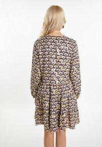 Trumpas rankovėmis suknelė, turinti tamsiai mėlyną fono spalvą ir gėlių raštą auksinės, grietinėlės ir mėlynos spalvos. Yra raukšlėtas sijonas ir suknelės uždarymas mygtukais gale.