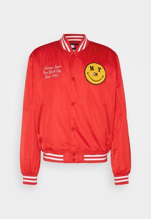 Rote Bomberjacke mit gestreiftem Kragen und Bündchen, besticktem Schriftzug „Tommy Jeans New York City Since 1985“ und gelbem NY-Smiley-Patch.