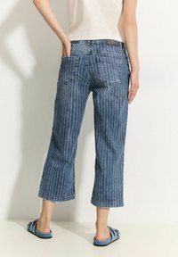 Jeans cortos a rayas azules con un ajuste holgado, que cuentan con dos bolsillos traseros y una cinturilla clásica. Combinados con calzado azul tipo slip-on.