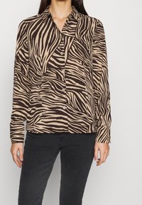 Beige- und braun gestreiftes Hemd mit Zebra-Muster, langen Ärmeln und Kragen, das eine leicht lockere Passform und geknöpfte Manschetten hat.