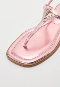 Rosa metallisk tångsandaler med fyrkantig tå, som har en dekorativ triangelformad logotyp på remmen och en platt sula.