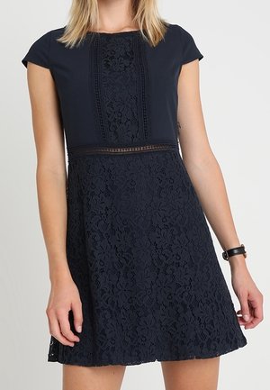 Robe en dentelle bleu marine avec des manches courtes à volants, motif floral, corsage texturé avec un panneau central et jupe évasée.