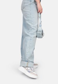 Jeans in denim azzurro chiaro con orli sfrangiati, abbinati a sneaker chunky multicolori con accenti bianchi, grigi e blu. Piccola borsa a tracolla.