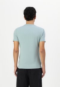 Lyseblå, kortærmet T-shirt lavet af blødt stof, med rund halsudskæring og en tætsiddende design, vist fra ryggen.
