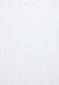 White shirt, lightweight cotton blend, with a smooth texture. Features a round neckline and raglan sleeves, minimalistic design.