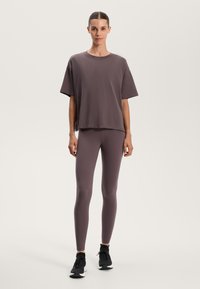 Lösa kortärmade skjortor i dämpad mauve, tillsammans med figurnära mauve leggings. Båda är gjorda av mjukt, elastiskt material. Svarta träningsskor.