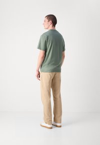 T-shirt en coton vert avec col rond, associé à un pantalon en coton beige et des baskets blanches. Design simple et sans ornements avec une coupe décontractée.
