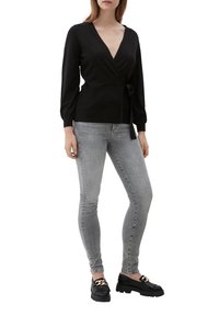 Schwarzer Wickelsweater mit langenÄrmeln, gerippter Textur und Bindeband in der Taille, kombiniert mit hellgrauen Skinny-Jeans und schwarzen Loafers.