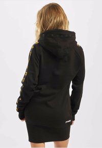 Čierna mikinová šaty s bočným brandingom v žltom texte, klokankovou vreckom, nastaviteľnou kapucňou s šnúrkou a slim fit dizajnom.