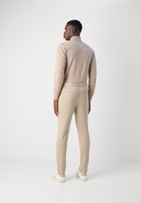 Bež turtleneck pulover, teksturirana tkanina, uske bež hlače, pogled straga, uparen s bijelim tenisicama s laganim bež detaljima.