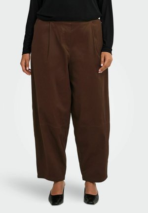 Personne portant un pantalon large marron ample assorti à un haut noir à manches longues et des chaussures noires à bout pointu.